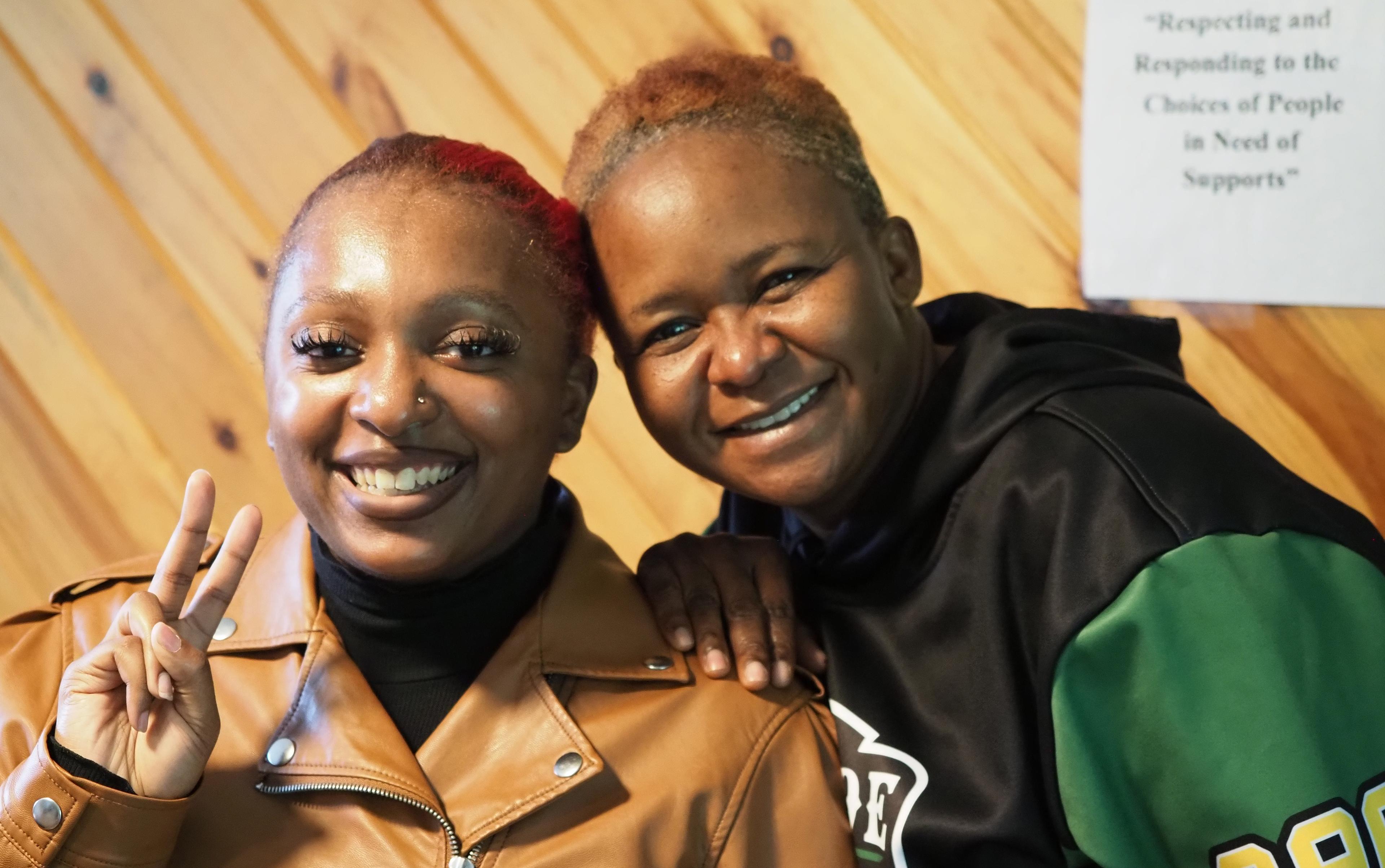 Two people smiling warmly at the camera, conveying a joyful and friendly atmosphere. One shows a peace sign.